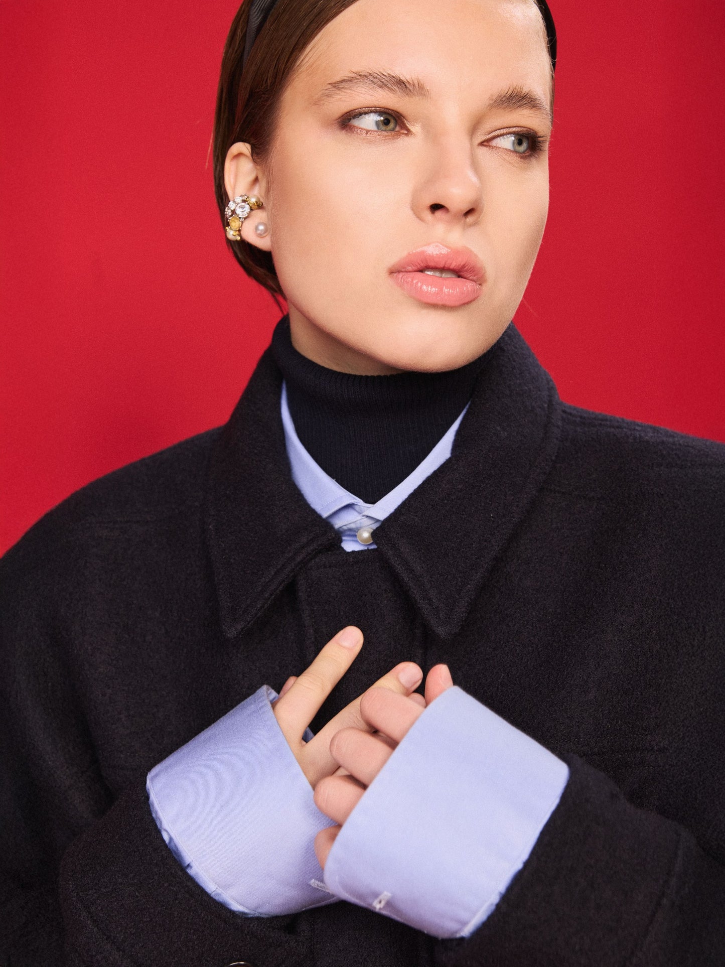 Woman wearing a dark blue jacket and blue turtleneck with light blue cuffs against a red background